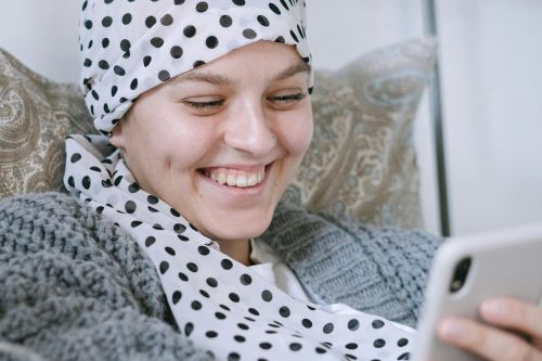 A woman with a polka dot scarf smiles while using her smartphone in bed.