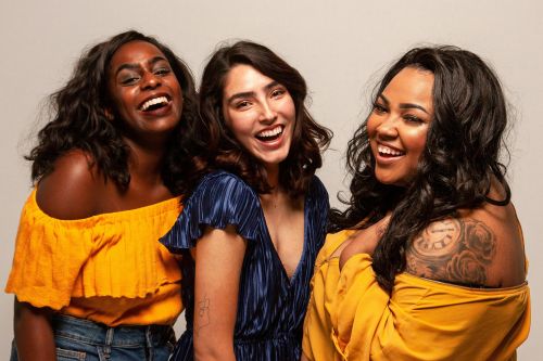 Joyful group of diverse women laughing together in bright outfits.