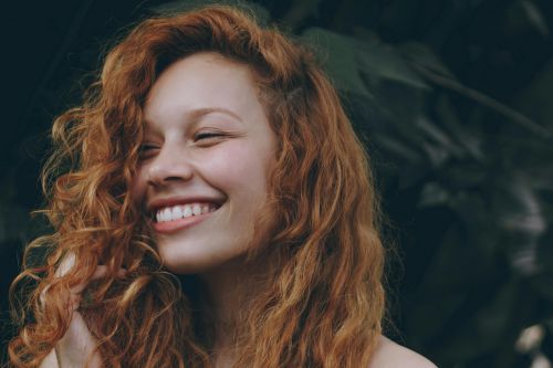 A candid portrait of a joyful woman with curly red hair, expressing natural beauty and happiness.